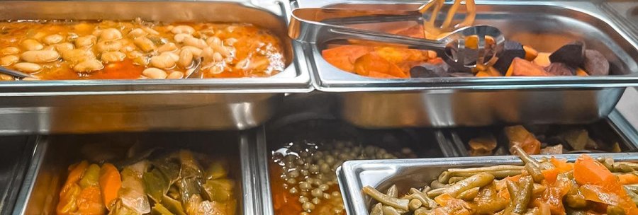 A buffet with various hot dishes in stainless steel containers, including beans, vegetables and stuffed eggplants., © Zauberküche, Stuttgart