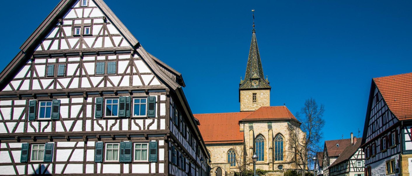 Half-timbered houses and a church in Kornwestheim against a blue sky. The architecture shows traditional construction methods with striking wooden beams., © Stuttgart-Marketing GmbH, Sarah Schmid