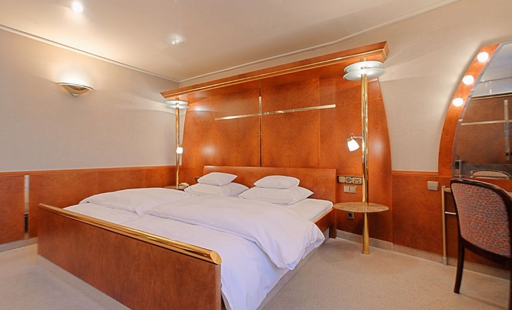 Elegantes Doppelzimmer mit großem Bett, Holzmöbeln und beleuchtetem Spiegel., © Hotel Royal