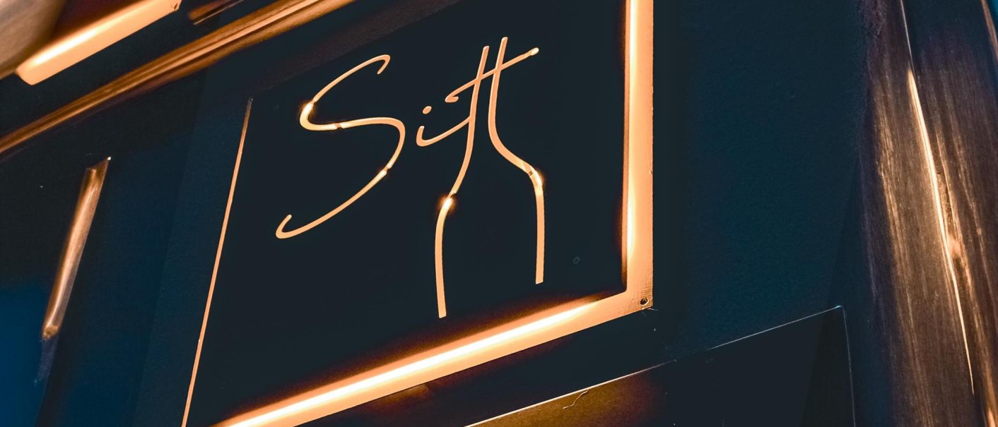 Neonschild mit der Aufschrift 'Sitt' und einer stilisierten Flasche in warmem Licht., © Sitt Wein, Stuttgart Neonschild mit der Aufschrift 'Sitt' und einer stilisierten Flasche in warmem Licht., © Sitt Wein, Stuttgart