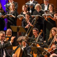 Ein Chor und Orchester in formeller Kleidung führen ein klassisches Musikstück auf. Der Dirigent leitet die Musiker, die konzentriert spielen und singen., © Holger Schneider Ein Chor und Orchester in formeller Kleidung führen ein klassisches Musikstück auf. Der Dirigent leitet die Musiker, die konzentriert spielen und singen., © Holger Schneider