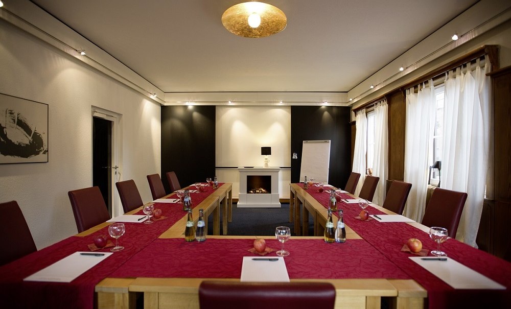 A conference room with a U-shaped table, red chairs, notepads, water bottles, and apples. A fireplace and a flip chart in the background., &copy; Hotel B&uuml;rkle