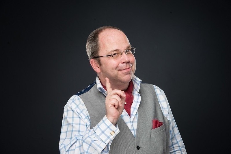 Ein Mann in kariertem Hemd und grauer Weste hebt den Zeigefinger, als ob er eine Idee hat. Der Hintergrund ist dunkel., &copy; Erlebnis Schmaus