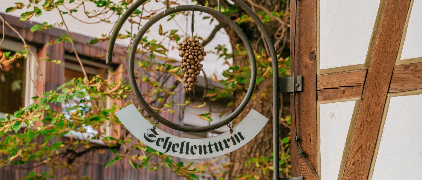 Ein Schild mit der Aufschrift 'Schellenturm' hängt an einem Fachwerkgebäude, umgeben von grünen Blättern., © © Stuttgart-Marketing GmbH, Thomas Niedermüller