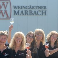 Sieben Personen heben lächelnd Weingläser vor einem Gebäude mit 'Weingärtner Marbach'-Logo., © Weingärtner Marbach e. G.