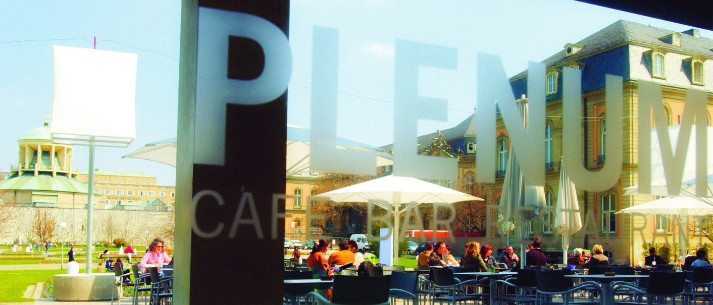People sit under parasols in the outdoor area of a café. Historical buildings can be seen in the background., © SMG