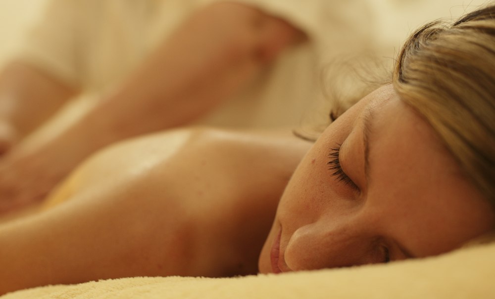 A woman is lying relaxed on a towel, receiving a back massage in a quiet, warm setting., © Badhotel Restaurant Stauferland A woman is lying relaxed on a towel, receiving a back massage in a quiet, warm setting., © Badhotel Restaurant Stauferland