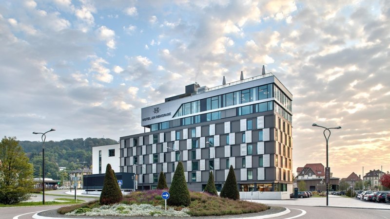 Modernes Hotelgebäude mit Glasfassade, umgeben von einem Kreisverkehr und gepflegter Landschaftsgestaltung, bei Sonnenuntergang., © Hotel am Remspark Modernes Hotelgebäude mit Glasfassade, umgeben von einem Kreisverkehr und gepflegter Landschaftsgestaltung, bei Sonnenuntergang., © Hotel am Remspark