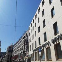 Ein modernes Geb&auml;ude mit dem Schriftzug 'Hotel Royal' unter blauem Himmel. Die Stra&szlig;e ist von weiteren Geb&auml;uden ges&auml;umt., &copy; Hotel Royal