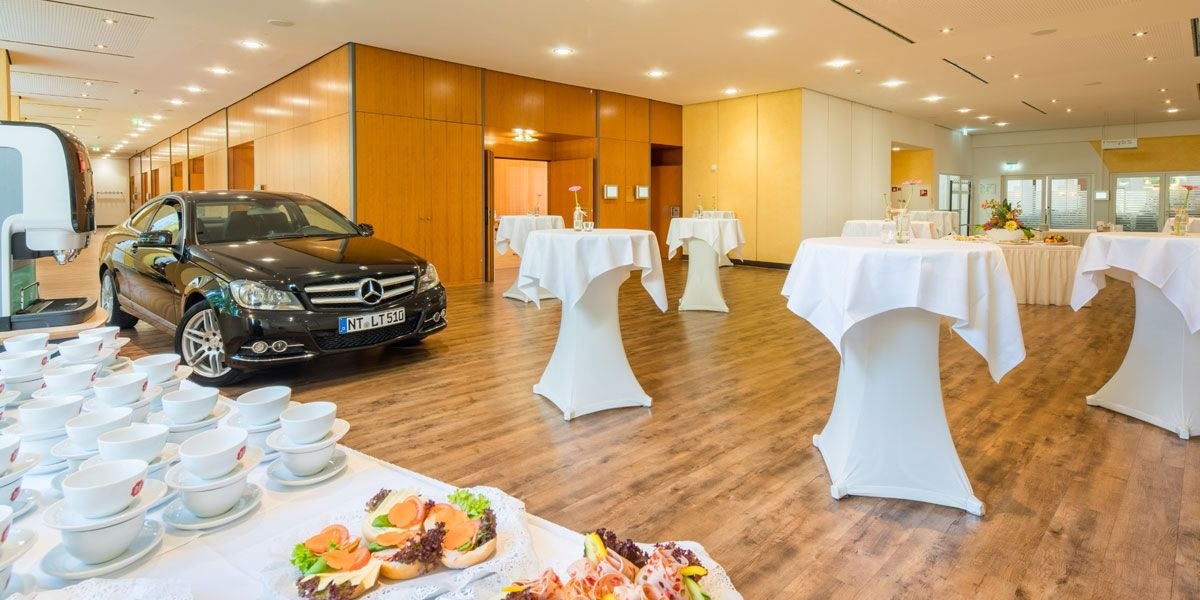 Ein Foyer mit einem schwarzen Auto, Stehtischen und einem Buffet mit Geschirr und Snacks., © Best Western Plus Hotel am Schlossberg