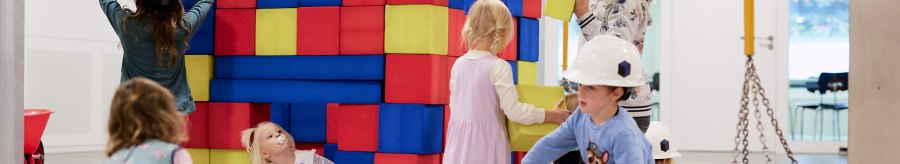 Children play on an indoor construction site with colorful foam blocks. They wear construction helmets and have fun building and playing., &copy; Julia Ochs