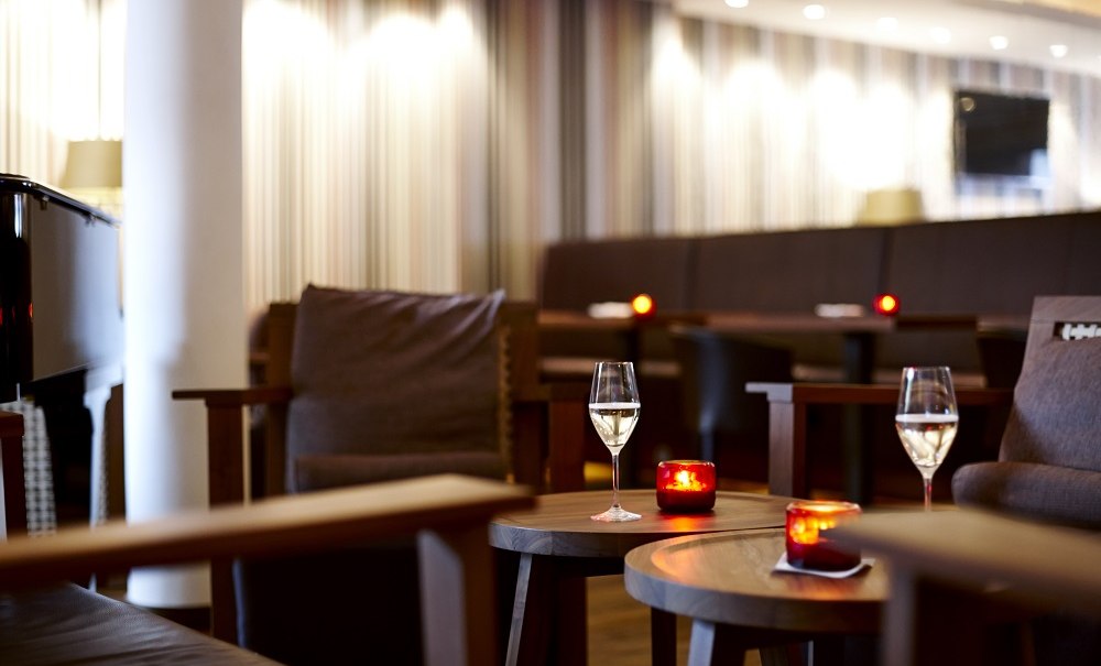 Elegante Hotelbar mit Weingläsern und Kerzen auf Holztischen, umgeben von bequemen Sesseln und gedämpfter Beleuchtung., © Waldhotel Stuttgart GmbH