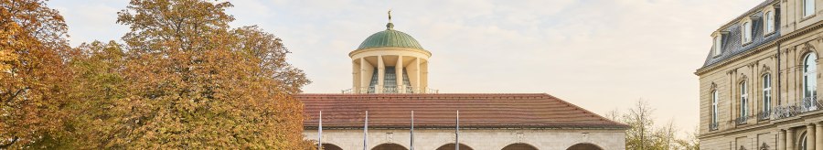 Historisches Gebäude mit Kuppel und Bögen, umgeben von herbstlichen Bäumen und gepflegtem Rasen., © Simon Sommer