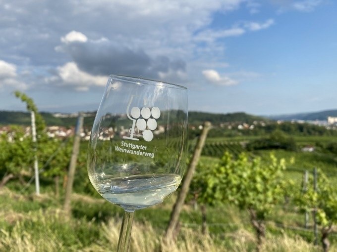Ein Weinglas mit der Aufschrift 'Stuttgarter Weinwanderweg' steht vor einer malerischen Landschaft mit Weinbergen und blauem Himmel., &copy; Weingenuss Stuttgart