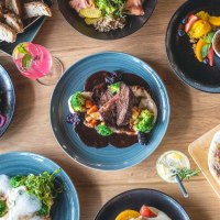 A table with various dishes: Meat with vegetables, salads, burgers with fries, bread and desserts. Drinks are also on display., © SatzDrei A table with various dishes: Meat with vegetables, salads, burgers with fries, bread and desserts. Drinks are also on display., © SatzDrei