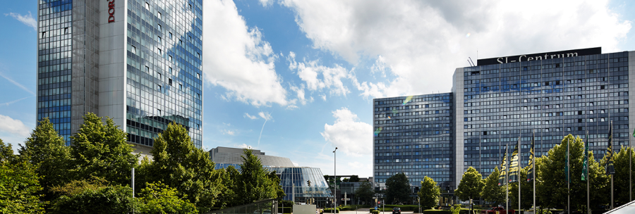 Moderne Gebäude des SI-Centrums mit Glasfassaden, umgeben von Bäumen, unter einem blauen Himmel mit Wolken., © Susanne Wegner Photography