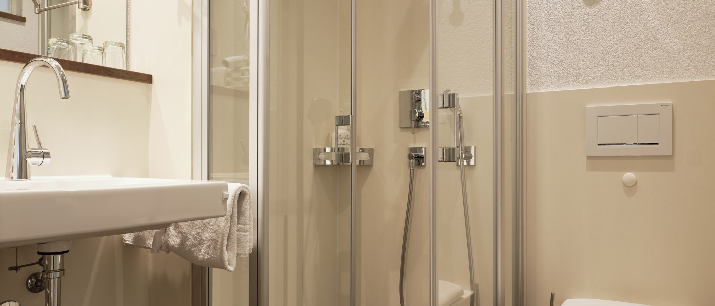 Modernes Badezimmer mit Glasdusche, Waschbecken und Toilette. Helle Wände, dunkler Boden, Spiegel und Handtuchhalter., © Badhotel Restaurant Stauferland