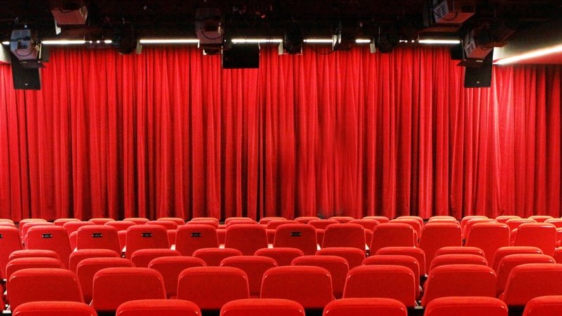 Leerer Theatersaal mit roten Stühlen und geschlossenem roten Vorhang, Beleuchtung und Lautsprechern an der Decke., © Sabine Haymann