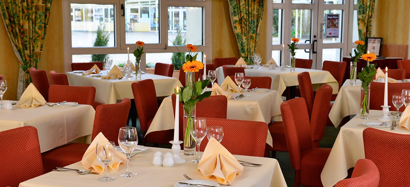 Elegant restaurant with red chairs, white tablecloths and flowers on the tables. Large windows in the background., © Amber Hotel Leonberg / Stuttgart Elegant restaurant with red chairs, white tablecloths and flowers on the tables. Large windows in the background., © Amber Hotel Leonberg / Stuttgart