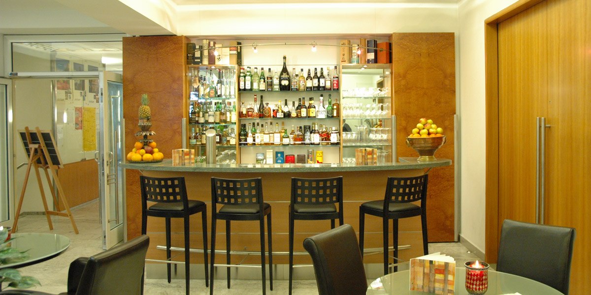Moderne Bar mit Tresen, Flaschenregal und vier Barhockern. Dekoriert mit Obstschalen und Gläsern. Elegantes Ambiente mit Holzelementen., © Hotel Unger