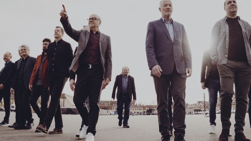 The SWR Big Band celebrates its 75th anniversary. A group of men in elegant clothing walk together across an open square., © SWR Big Band The SWR Big Band celebrates its 75th anniversary. A group of men in elegant clothing walk together across an open square., © SWR Big Band