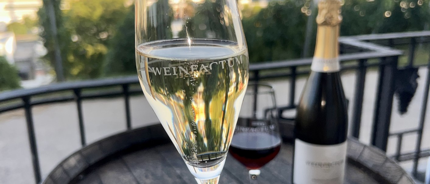 Ein Sektglas mit der Aufschrift 'Weinfactum' steht auf einem Tisch im Freien, daneben eine Flasche und ein Weinglas., © Weinfactum Bad Cannstatt Ein Sektglas mit der Aufschrift 'Weinfactum' steht auf einem Tisch im Freien, daneben eine Flasche und ein Weinglas., © Weinfactum Bad Cannstatt