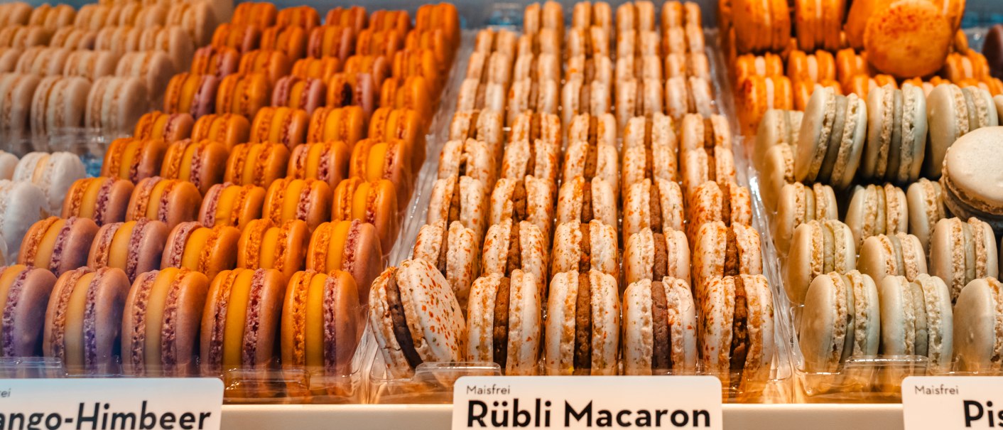 Macarons in verschiedenen Geschmacksrichtungen wie Vanille, Rübli und Aperol-Orange in einer Auslage präsentiert., © SMG, Sarah Schmid