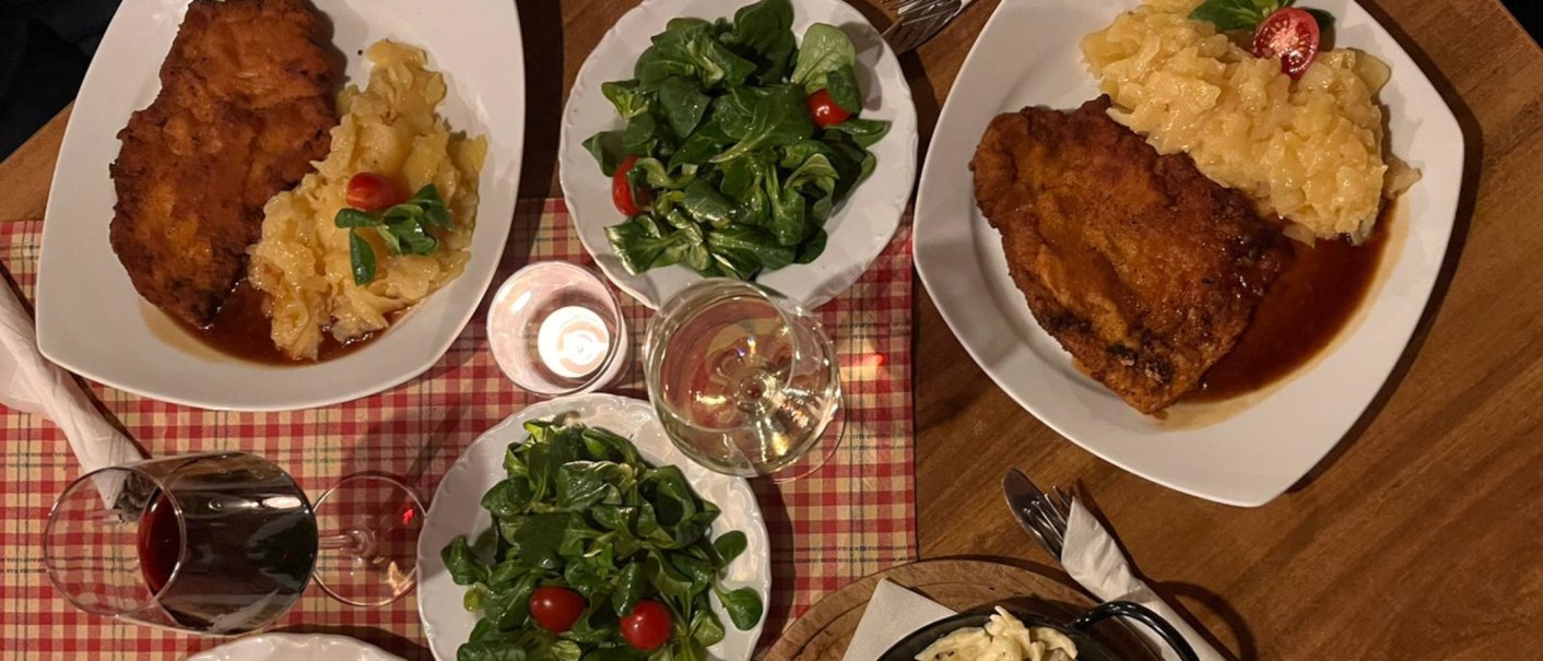 Two plates with schnitzel, potato salad and green salad. Served with red and white wine on a checkered tablecloth., &copy; Weinhof Zai&szlig;