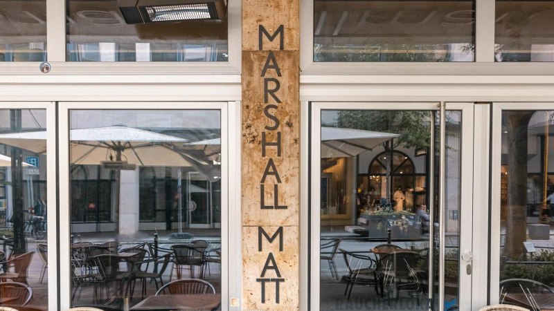 Eingang eines Cafés mit dem Namen Marshall Matt. Glasfront mit Spiegelung von Tischen, Stühlen und Sonnenschirmen im Außenbereich., © Stuttgart Marketing GmbH, Sarah Schmid