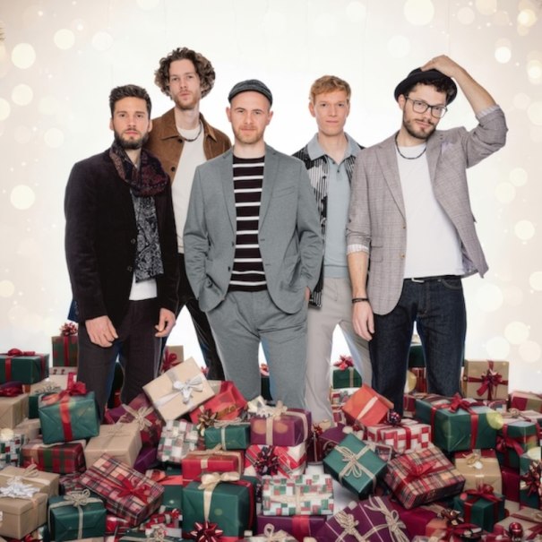 Five men pose in front of a festive background with numerous gifts. They are wearing fashionable clothes and look relaxed and cheerful., © Renitenztheater Stuttgart e.V. Five men pose in front of a festive background with numerous gifts. They are wearing fashionable clothes and look relaxed and cheerful., © Renitenztheater Stuttgart e.V.