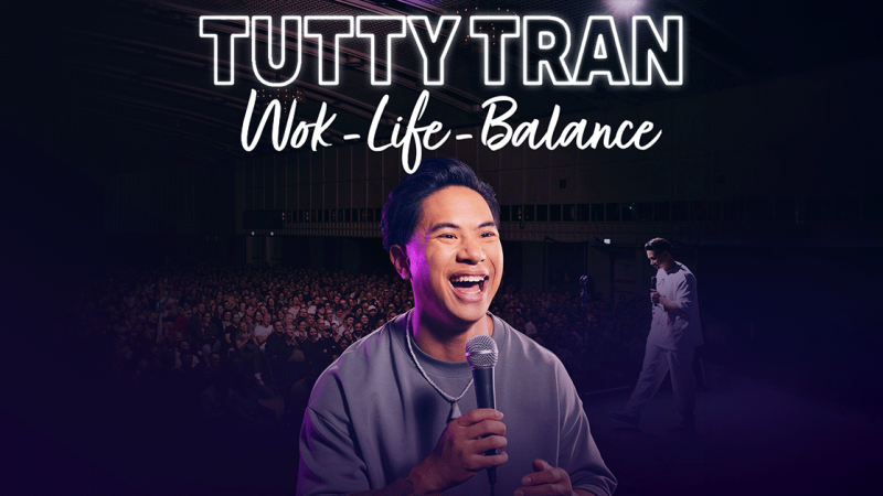 Ein Comedian steht lachend mit Mikrofon vor einem gro&szlig;en Publikum. Der Schriftzug 'TUTTY TRAN - Wok-Life-Balance' ist oben zu sehen., &copy; links im Bild
