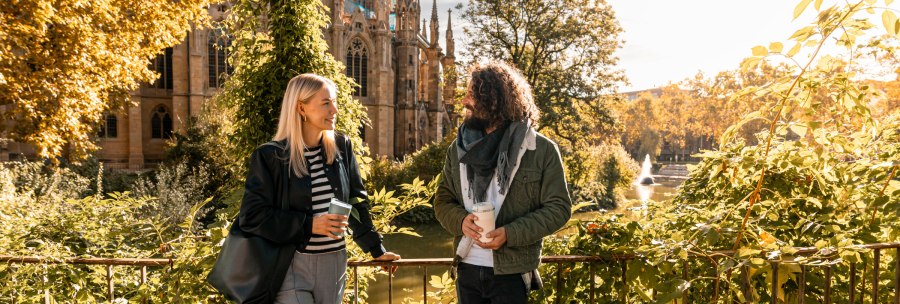 Two people are talking in front of St. John's Church on the Feuersee, surrounded by autumn leaves and sunshine., &copy; SMG, Sarah Schmid
