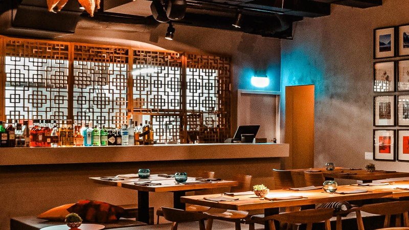 Stilvolles Restaurant mit Holztischen, dekorativen Gittern und einer Bar. An der Wand hängen gerahmte Bilder, die Atmosphäre ist warm und einladend., © Breitengrad17 Stuttgart