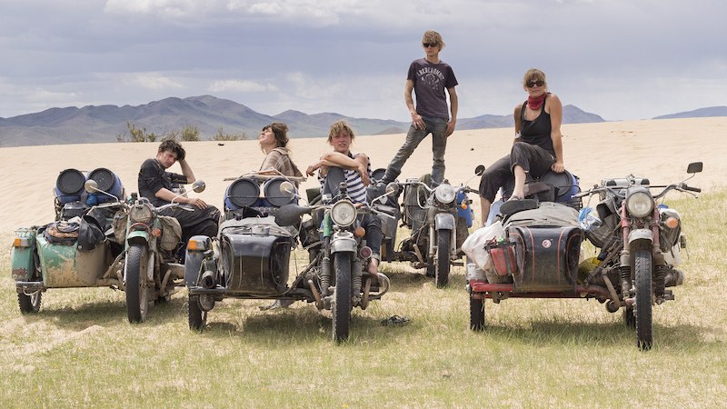 Fünf Personen posieren mit Motorrädern in einer Wüstenlandschaft. Der Himmel ist bewölkt, im Hintergrund sind Berge zu sehen., © Theaterhaus Stuttgart e.V.