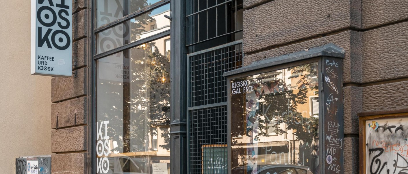 Ein Kiosk mit der Aufschrift 'Kiosko Kaffee und Kiosk'. Die Fassade ist mit Graffiti bedeckt, und das Schaufenster spiegelt die Umgebung wider., © SMG, Sarah Schmid