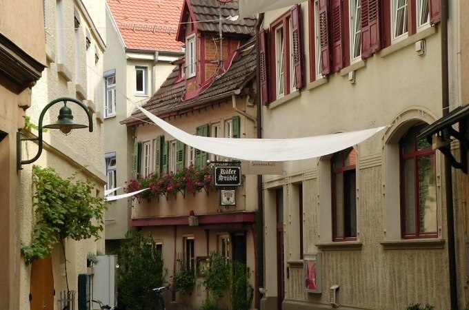 Narrow alley with historic buildings, flowers on the windows and white awnings. A sign points to a restaurant., © Cool-Tours StattReisen Narrow alley with historic buildings, flowers on the windows and white awnings. A sign points to a restaurant., © Cool-Tours StattReisen