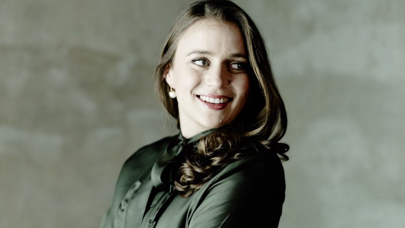 Eine Frau mit langen Haaren und dunkler Bluse l&auml;chelt und blickt zur Seite. Der Hintergrund ist grau und unscharf., &copy; Internationale Hugo-Wolf-Akademie