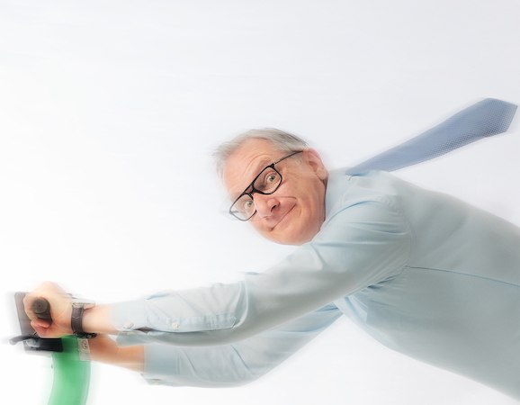 Ein Mann mit Brille f&auml;hrt dynamisch auf einem gr&uuml;nen E-Scooter, seine Krawatte weht im Wind. Der Hintergrund ist wei&szlig;., &copy; Renitenztheater Stuttgart e.V.