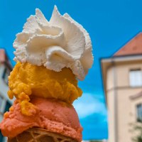 Eine Eist&uuml;te mit drei Kugeln und Sahne vor einem blauen Himmel und unscharfen Geb&auml;uden im Hintergrund., &copy; Kesselgl&uuml;ck
