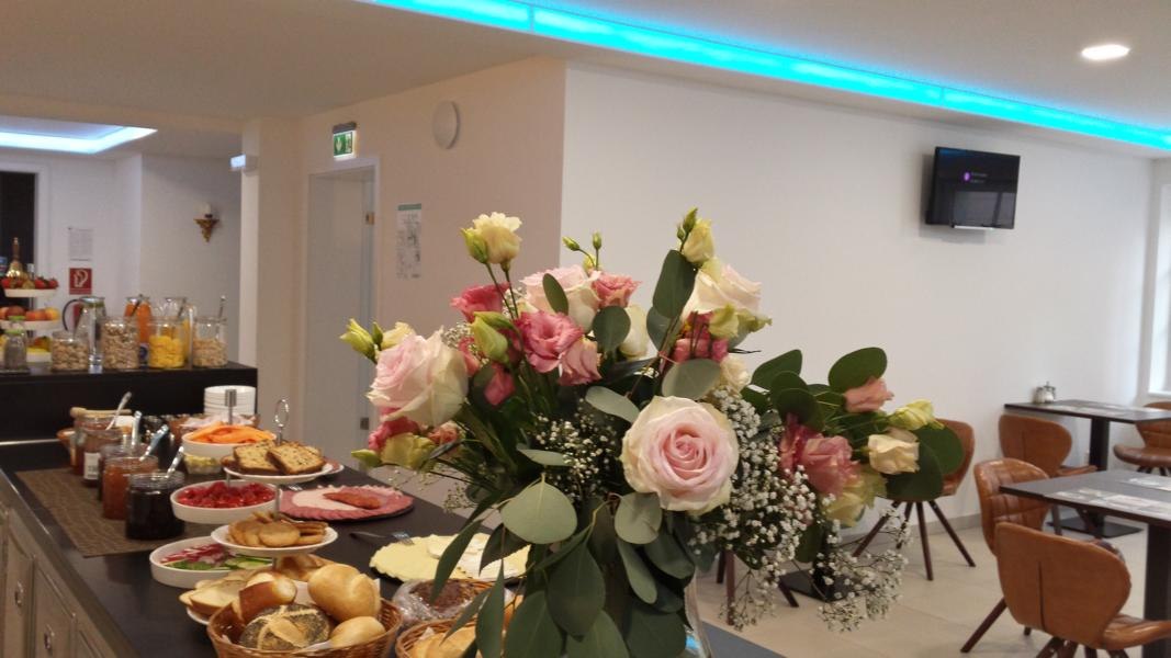 Frühstücksbüffet mit Blumenstrauß, Brotsorten, Aufschnitt und Marmeladen in einem hellen Raum mit modernen Möbeln., © TOMAS