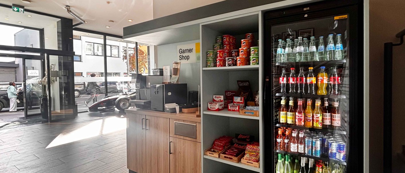 Ein kleiner Ladenbereich namens Garner Shop mit Snacks und Getr&auml;nken in einem modernen Geb&auml;ude. Ein K&uuml;hlschrank ist mit verschiedenen Getr&auml;nken gef&uuml;llt., &copy; Novum Hospitality