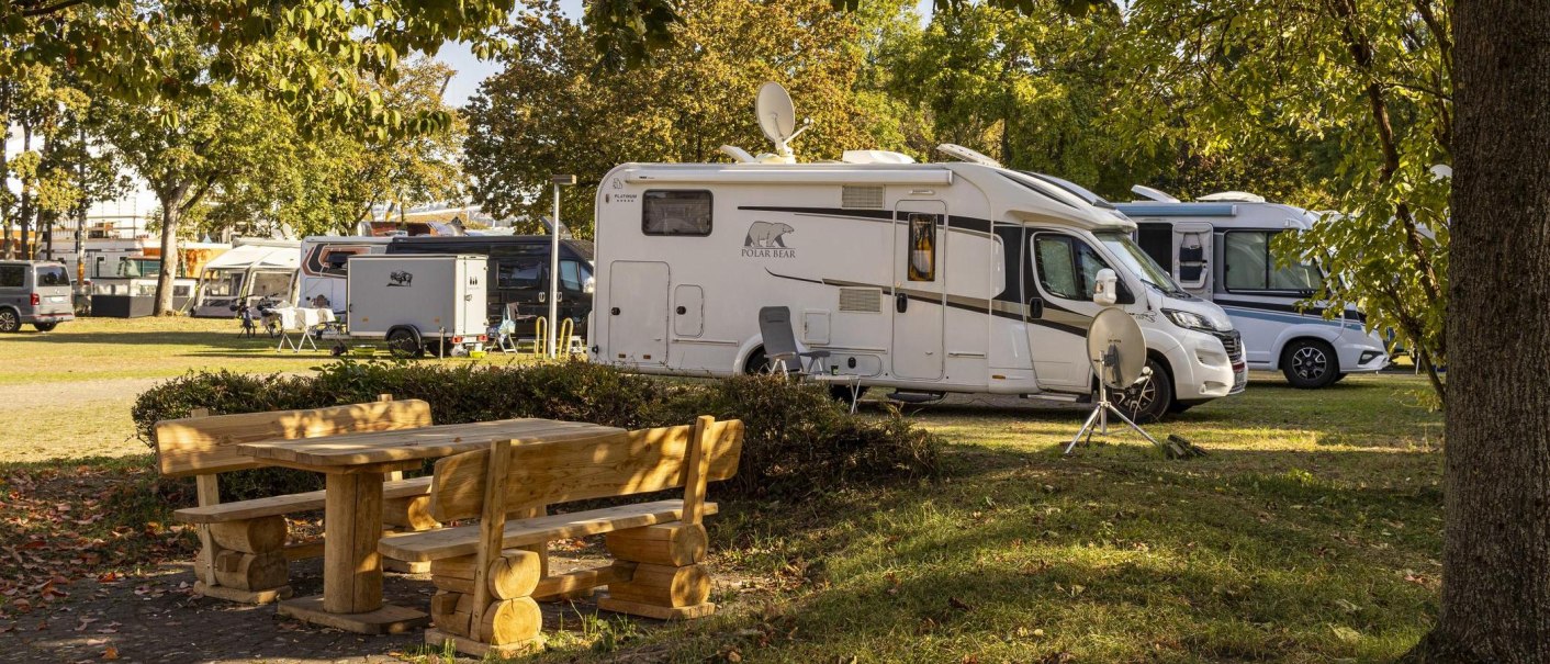 Wohnmobile auf einem sonnigen Campingplatz, umgeben von Bäumen. Im Vordergrund steht ein Holztisch mit Bänken., © Stuttgart-Marketing GmbH, Sarah Schmid Wohnmobile auf einem sonnigen Campingplatz, umgeben von Bäumen. Im Vordergrund steht ein Holztisch mit Bänken., © Stuttgart-Marketing GmbH, Sarah Schmid