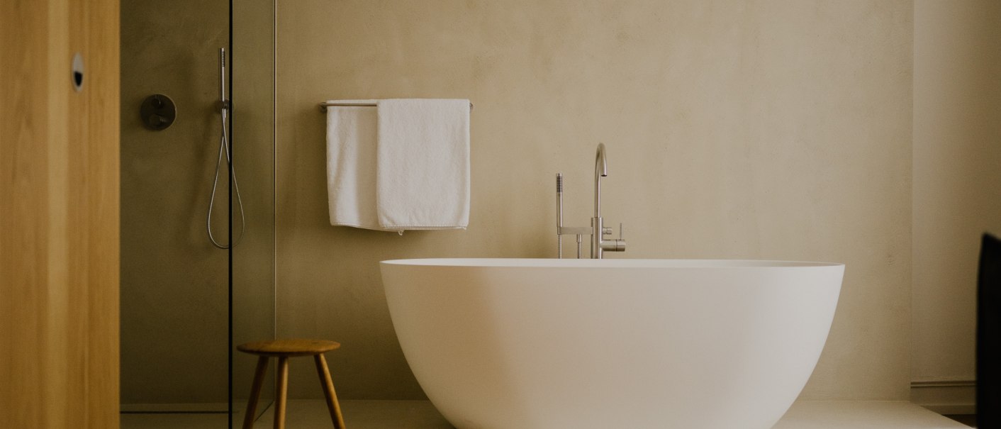 Modernes Badezimmer mit freistehender Badewanne, Glasdusche, Handtuchhalter und kleinem Holzstuhl auf Holzboden., © Peter Oliver Wolff / DAS EDITH