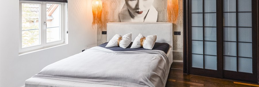 Modernes Hotelzimmer mit großem Bett, Wandbild einer Frau, zwei Hängelampen und Holzfußboden., © Zauberlehrling Modernes Hotelzimmer mit großem Bett, Wandbild einer Frau, zwei Hängelampen und Holzfußboden., © Zauberlehrling