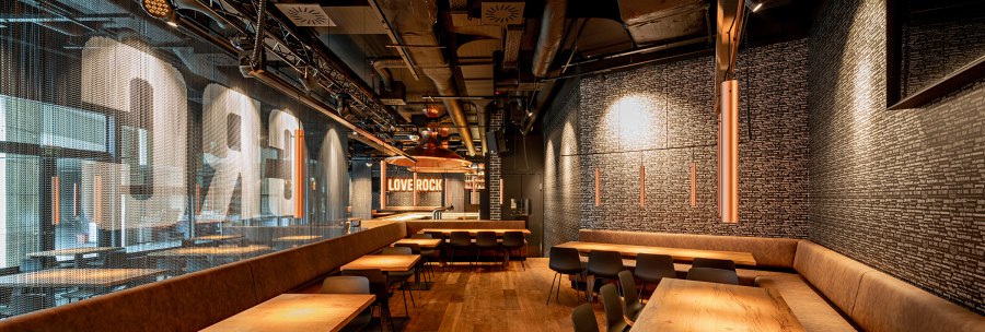 Modernes Café mit Holztischen, gepolsterten Bänken und dem Schriftzug 'LOVE ROCK' an der Wand., © Maks Richter Modernes Café mit Holztischen, gepolsterten Bänken und dem Schriftzug 'LOVE ROCK' an der Wand., © Maks Richter
