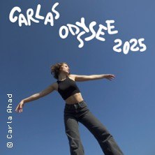Frau in schwarzer Kleidung posiert vor blauem Himmel. Text 'Carlas Odyssee 2025' oben im Bild., © links im Bild Frau in schwarzer Kleidung posiert vor blauem Himmel. Text 'Carlas Odyssee 2025' oben im Bild., © links im Bild