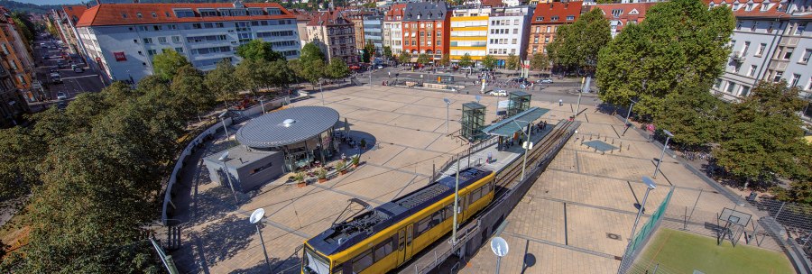 Aerial view of Marienplatz in Stuttgart. A yellow streetcar passes by, surrounded by trees and buildings. The square is lively and sunny., &copy; Stuttgart-Marketing GmbH