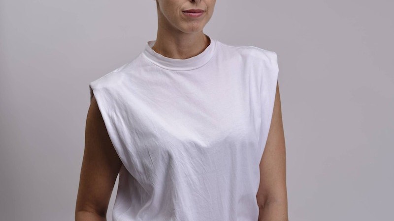A person with short hair wears a white sleeveless top and stands in front of a gray background., &copy; Renitenztheater Stuttgart e.V.