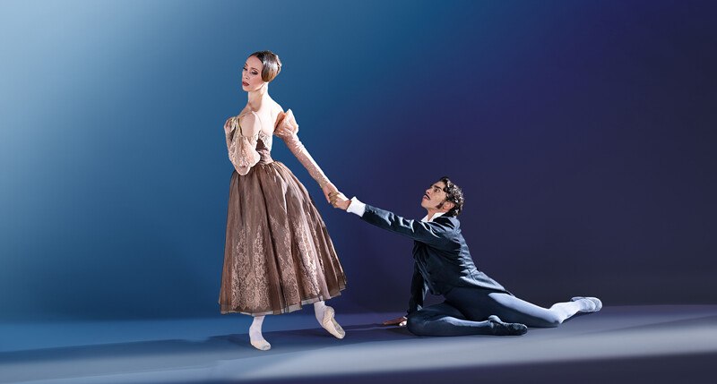 Zwei Ballettt&auml;nzer in dramatischer Pose: Eine Frau in einem eleganten Kleid steht, w&auml;hrend ein Mann in Anzug kniet und ihre Hand h&auml;lt., &copy; W&uuml;rttembergische Staatstheater Stuttgart