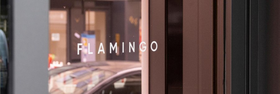 Weißer Schriftzug "FLAMINGO" in Großbuchstaben auf der verspiegelten Glasfront der Bar, © SMG, Sarah Schmid Weißer Schriftzug "FLAMINGO" in Großbuchstaben auf der verspiegelten Glasfront der Bar, © SMG, Sarah Schmid